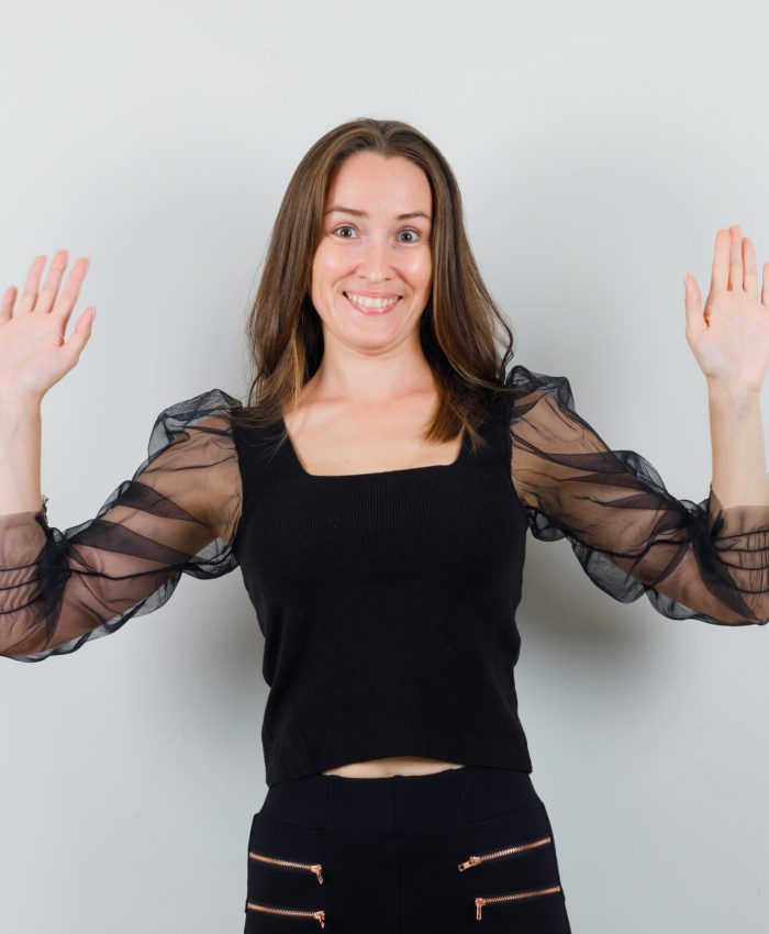 beautiful woman in black blouse raising hands up and looking merry , front view.